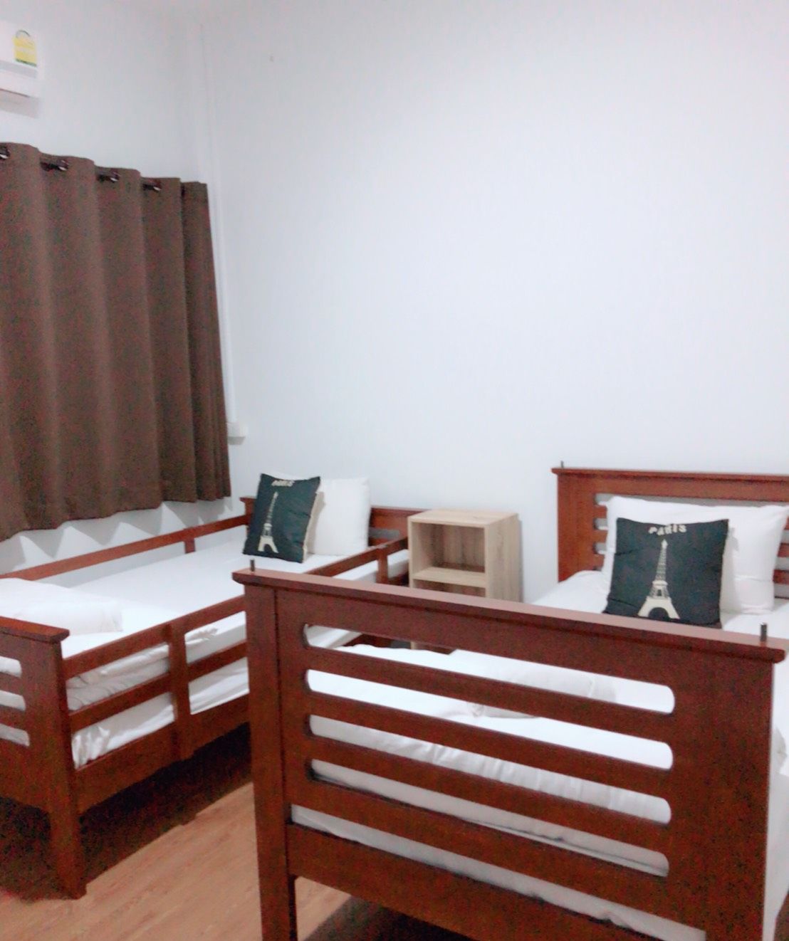 A dormitory room with two wooden bunk beds, a small wooden nightstand, and a white wall.