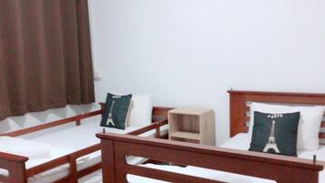 A dormitory room with two wooden bunk beds, a small wooden nightstand, and a white wall.