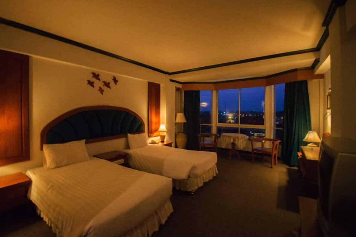A hotel room with two beds, a small table, chairs, and a view of the city at night.