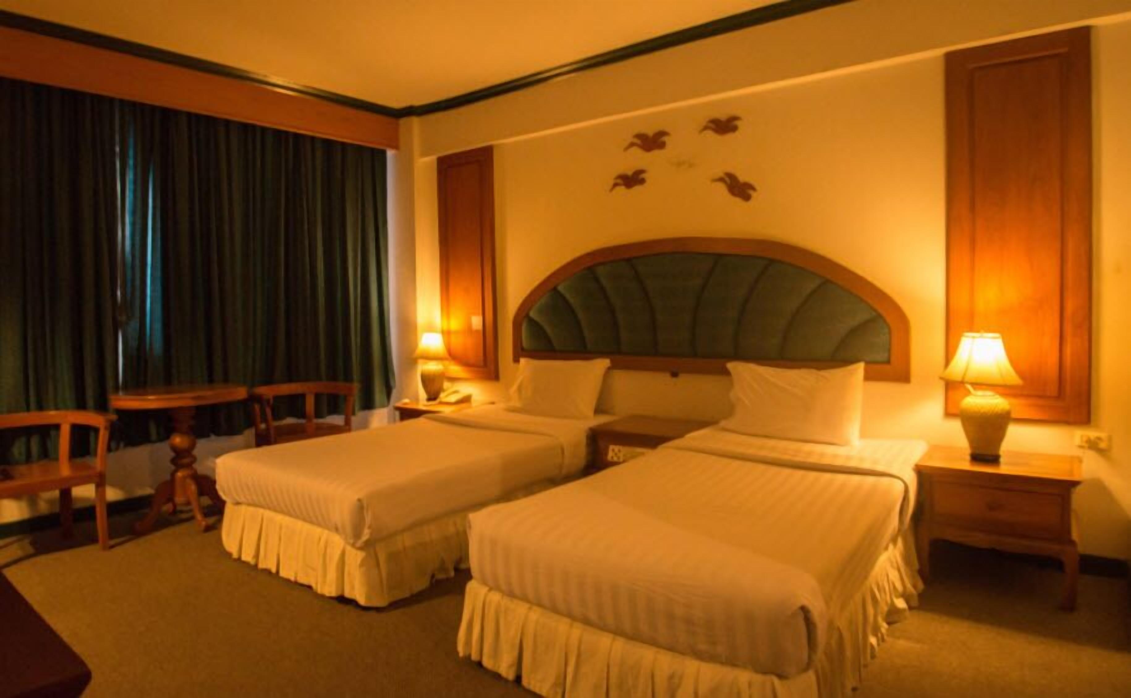 A hotel room with two single beds, a desk, a chair, and a lamp.