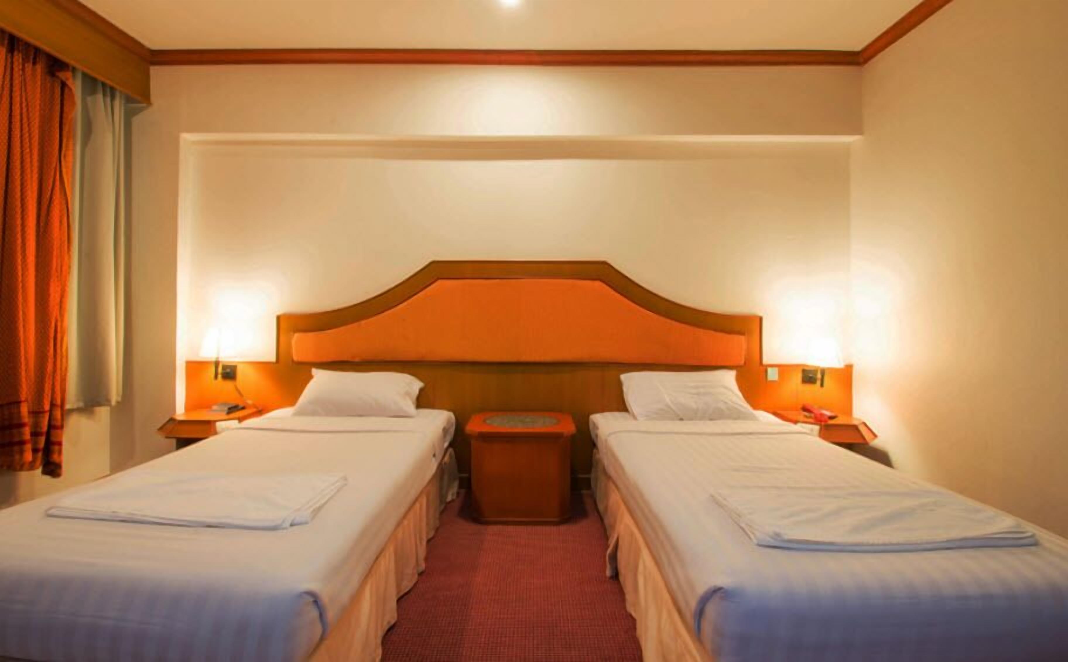 Une chambre d’hôtel avec deux lits simples, une tête de lit en bois, une moquette rouge et deux lampes de chevet.