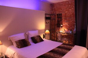 Ein Hotelzimmer mit Backsteinwand, einem Bett mit weißer Bettwäsche, einem Nachttisch mit Lampe und einem kleinen Tisch ebenfalls mit Lampe.