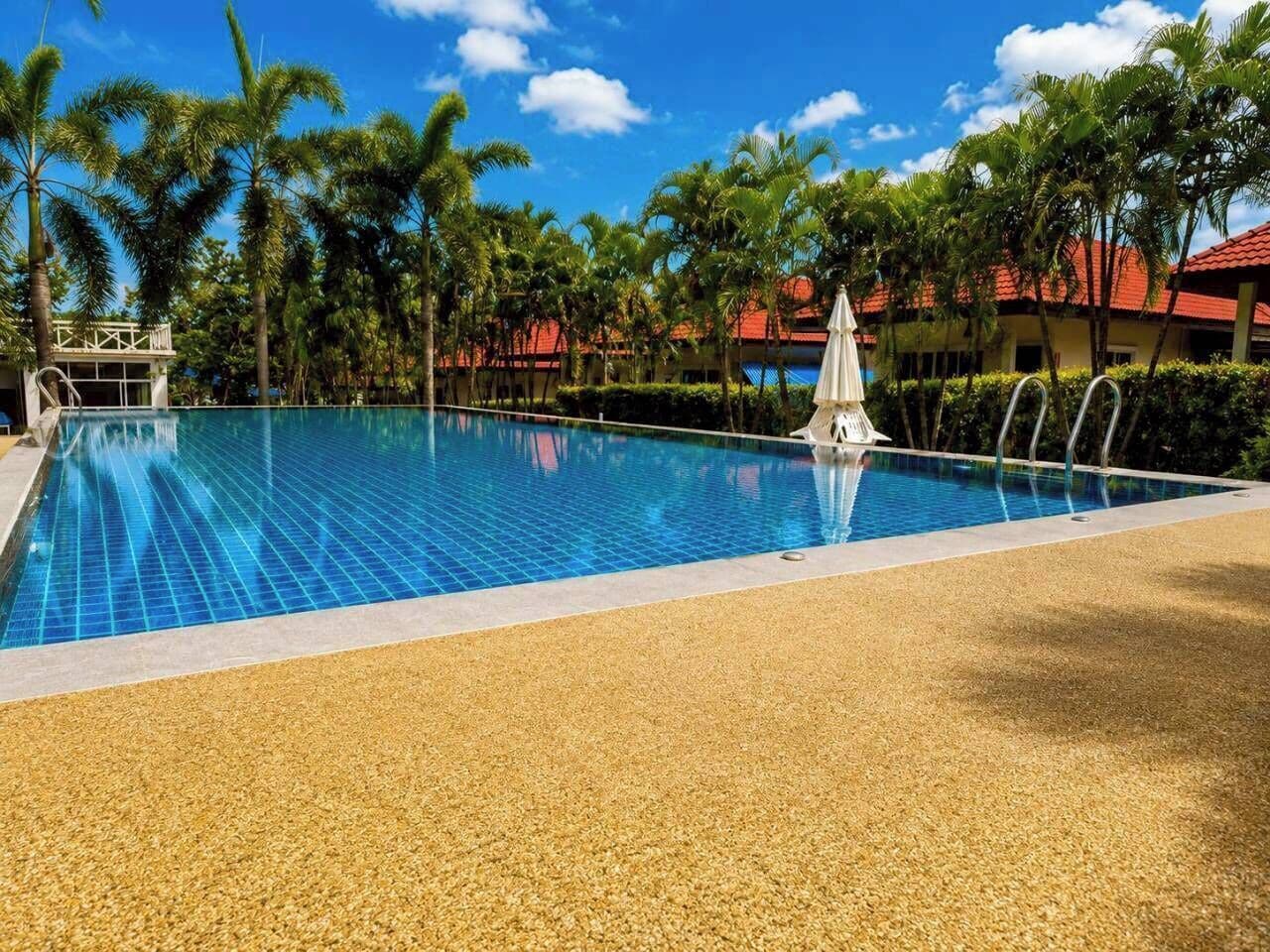 Une piscine dont le fond est recouvert de carreaux, entourée de palmiers et, au fond, un bâtiment avec un toit rouge.