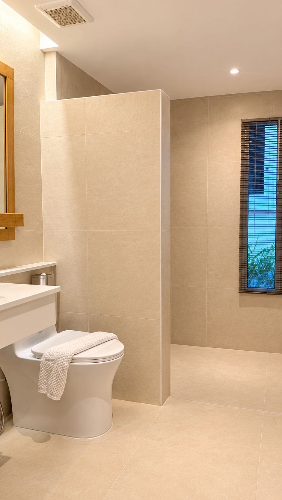 A modern bathroom with a toilet, shower, and a window with blinds.