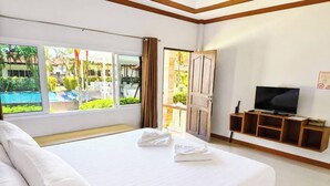 A hotel room with a large bed, a television, and a view of a swimming pool and greenery. - Phuket Airport Villa (Sa Khu)