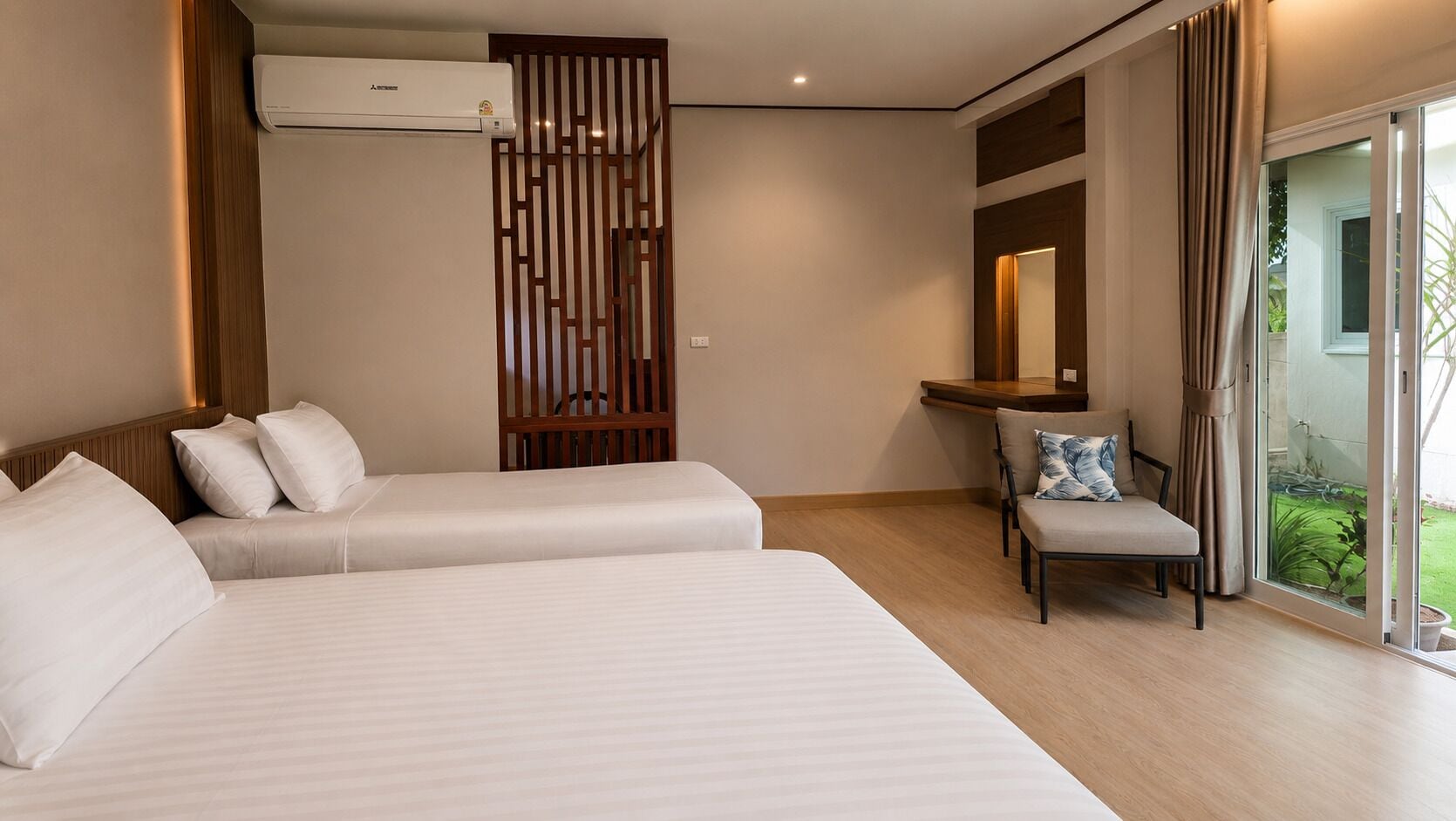 Une chambre d’hôtel avec deux lits, un coin salon, une cloison en bois et une porte-fenêtre coulissante donnant sur l’extérieur.