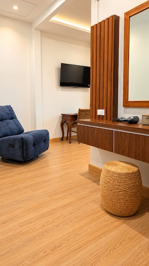 Una habitación moderna con un sofá azul, un armario de madera, un televisor y un reposapiés de mimbre.