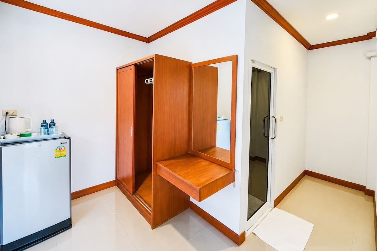 Een compacte kamer met een kitchenette, een houten garderobe en een glazen deur naar een douchecel.
