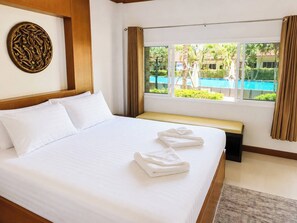 A hotel room with a bed, a bench, a window with curtains, and a view of a pool.