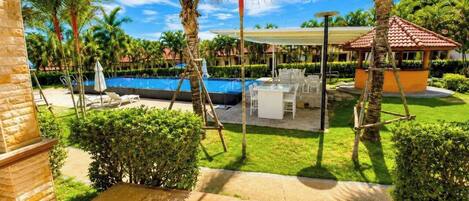 A pool area with lounge chairs, a covered seating area, and palm trees.
