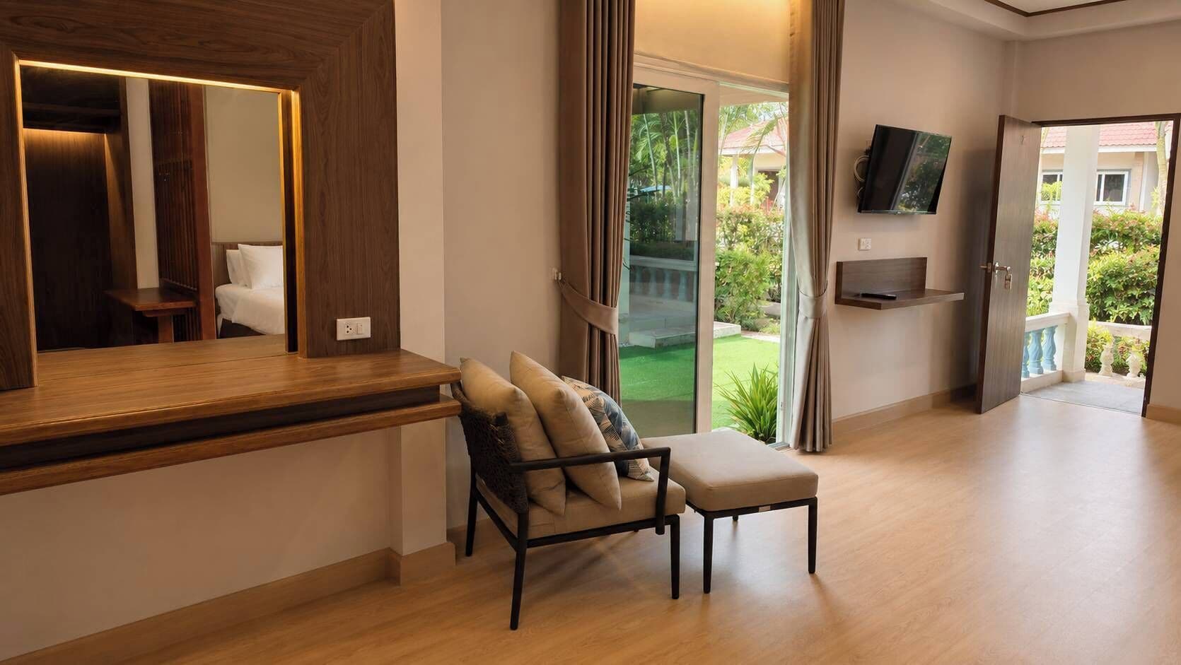 A modern room with a wooden desk, a cushioned chair, a television mounted on the wall, and a sliding glass door leading to a balcony.