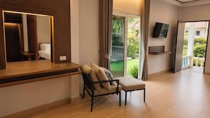 Una habitación moderna con un escritorio de madera, una silla acolchada, un televisor montado en la pared y una puerta corrediza de vidrio que da a un balcón.