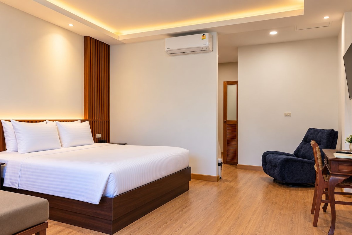 Una habitación de hotel con cama, mesita de noche, silla, escritorio y aire acondicionado.