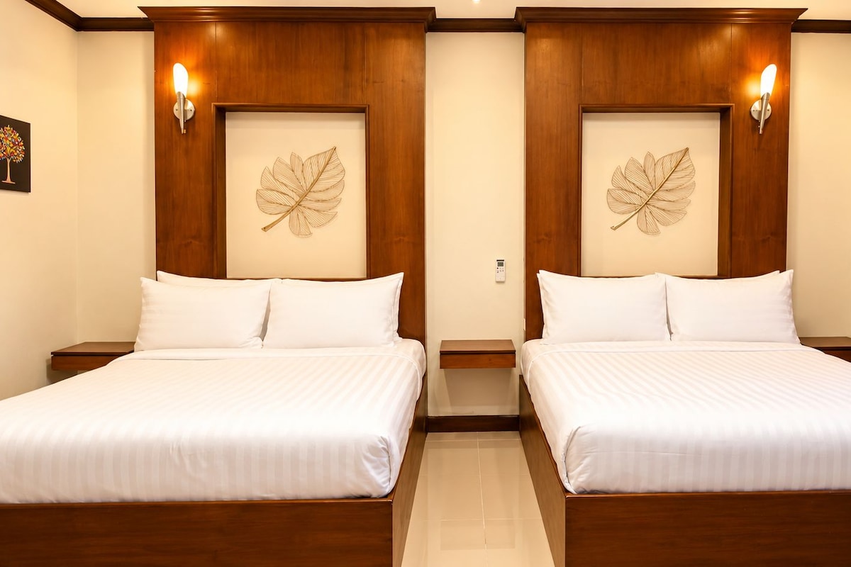 Habitación de hotel con dos camas, cabeceros de madera, lámparas fijadas a la pared y un ventanal con cortinas.