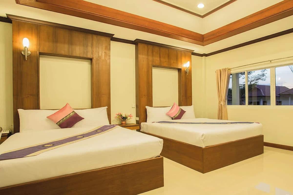 Een hotelkamer met twee bedden, houten hoofdborden en een groot raam met gordijnen.