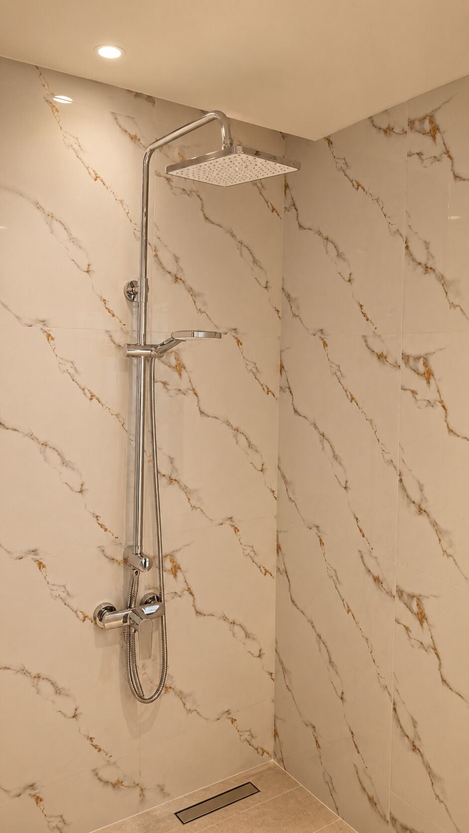 A shower with a handheld showerhead and a rain shower head, set against marble-patterned walls.