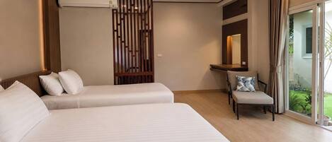 Quarto de hotel com duas camas, uma escrivaninha, uma cadeira, uma janela grande e uma porta de vidro deslizante que dá para uma varanda.