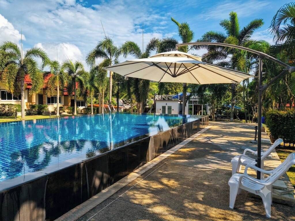 Une piscine avec un espace de détente, des palmiers et un ciel dégagé.