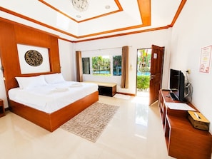 A bedroom with a large bed, a desk with a computer, a TV, and a window with a view of a pool. - Phuket Airport Villa (Sa Khu)