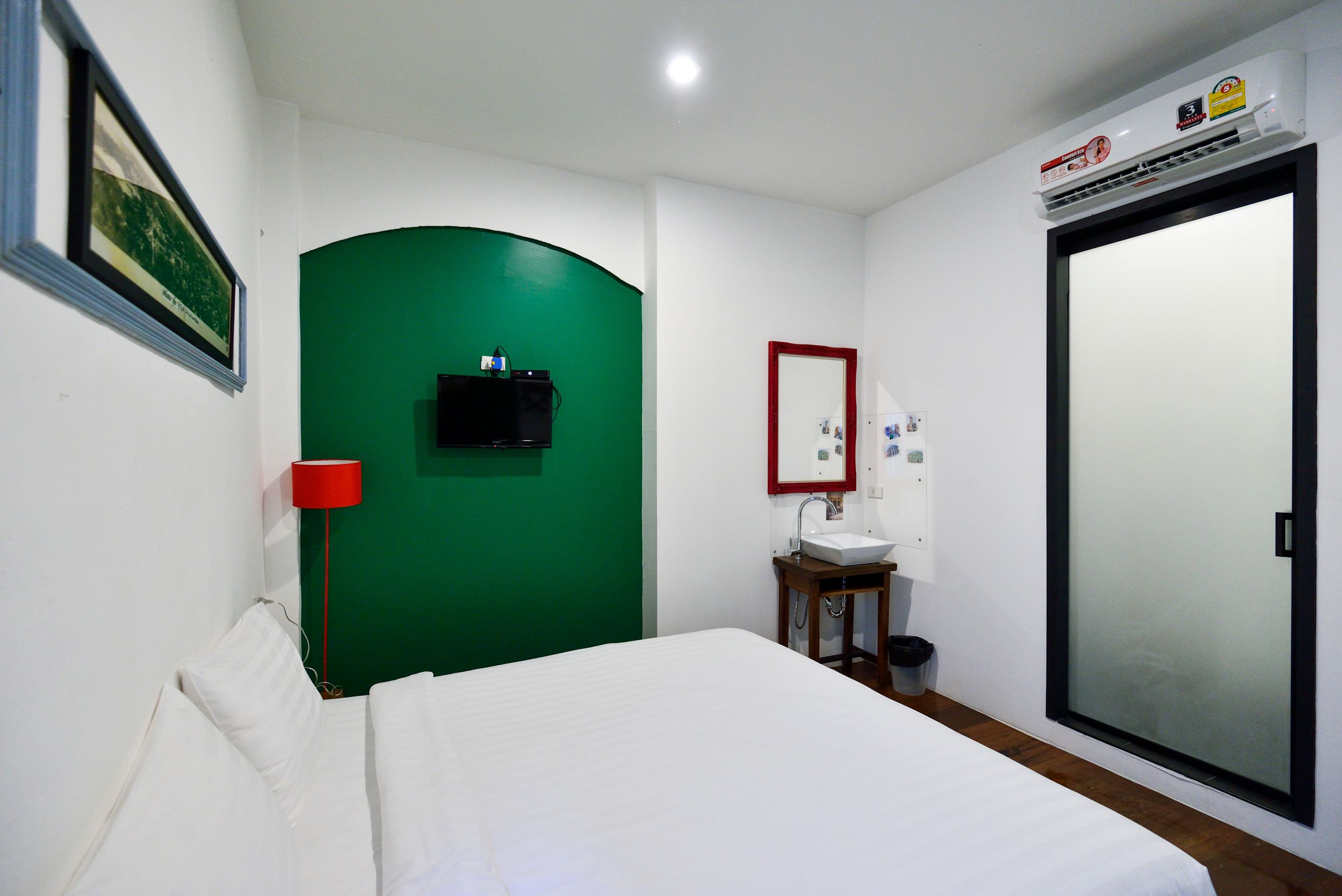A bedroom with a bed, a green wall, a small table with a sink, and a mirror.