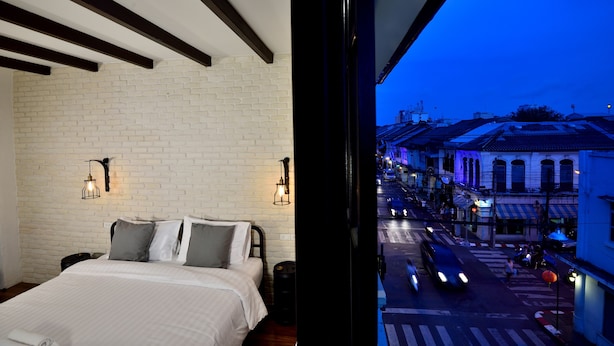 Un dormitorio con pared de ladrillo, una cama con almohadas y dos luces fijadas a la pared.