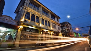 Un edificio histórico con ventanas de arco y un balcón, situado en una calle con estelas de luz dejadas por vehículos en movimiento.