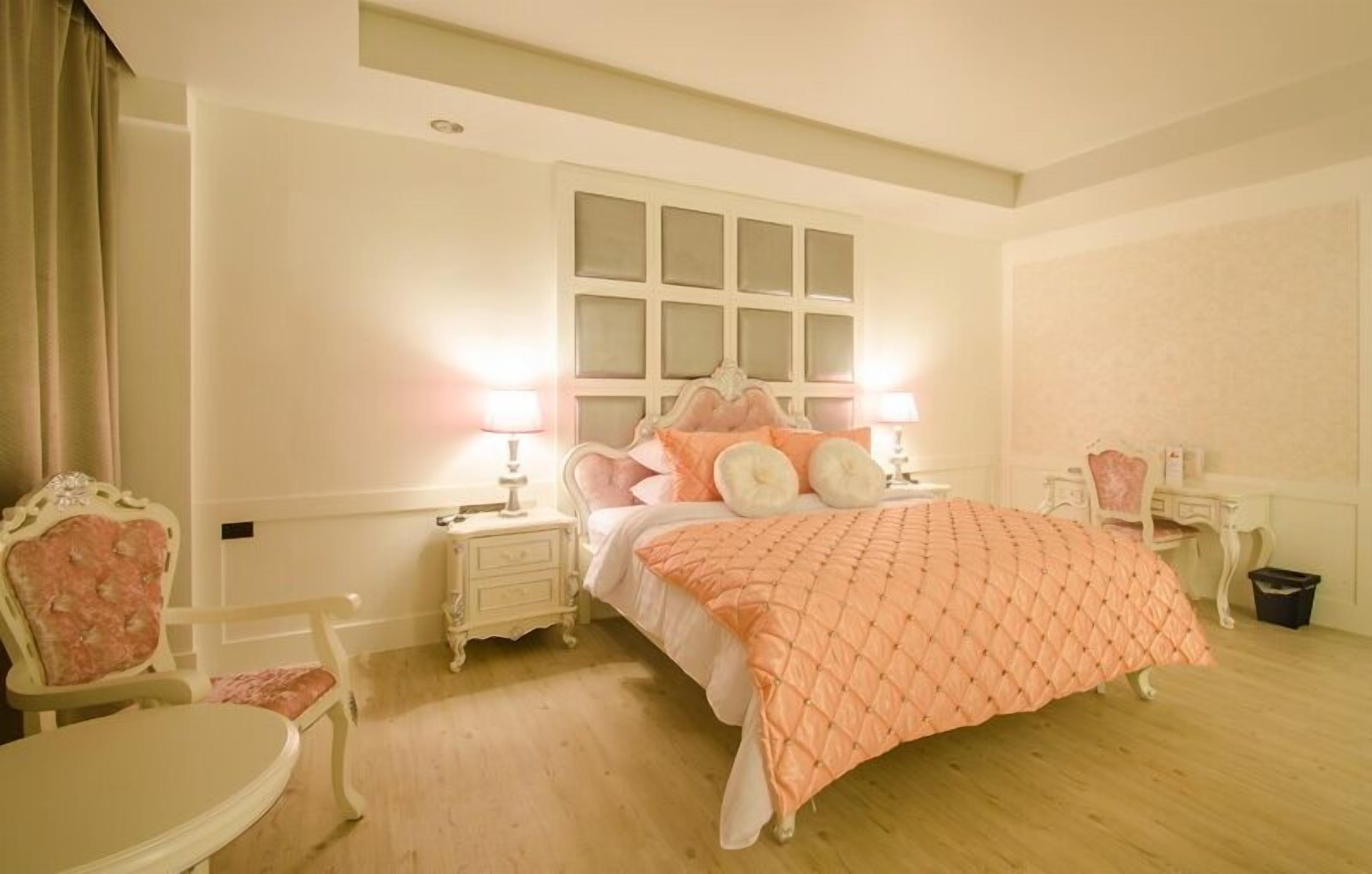 A bedroom with a large bed, two bedside tables, a chair, and a desk.