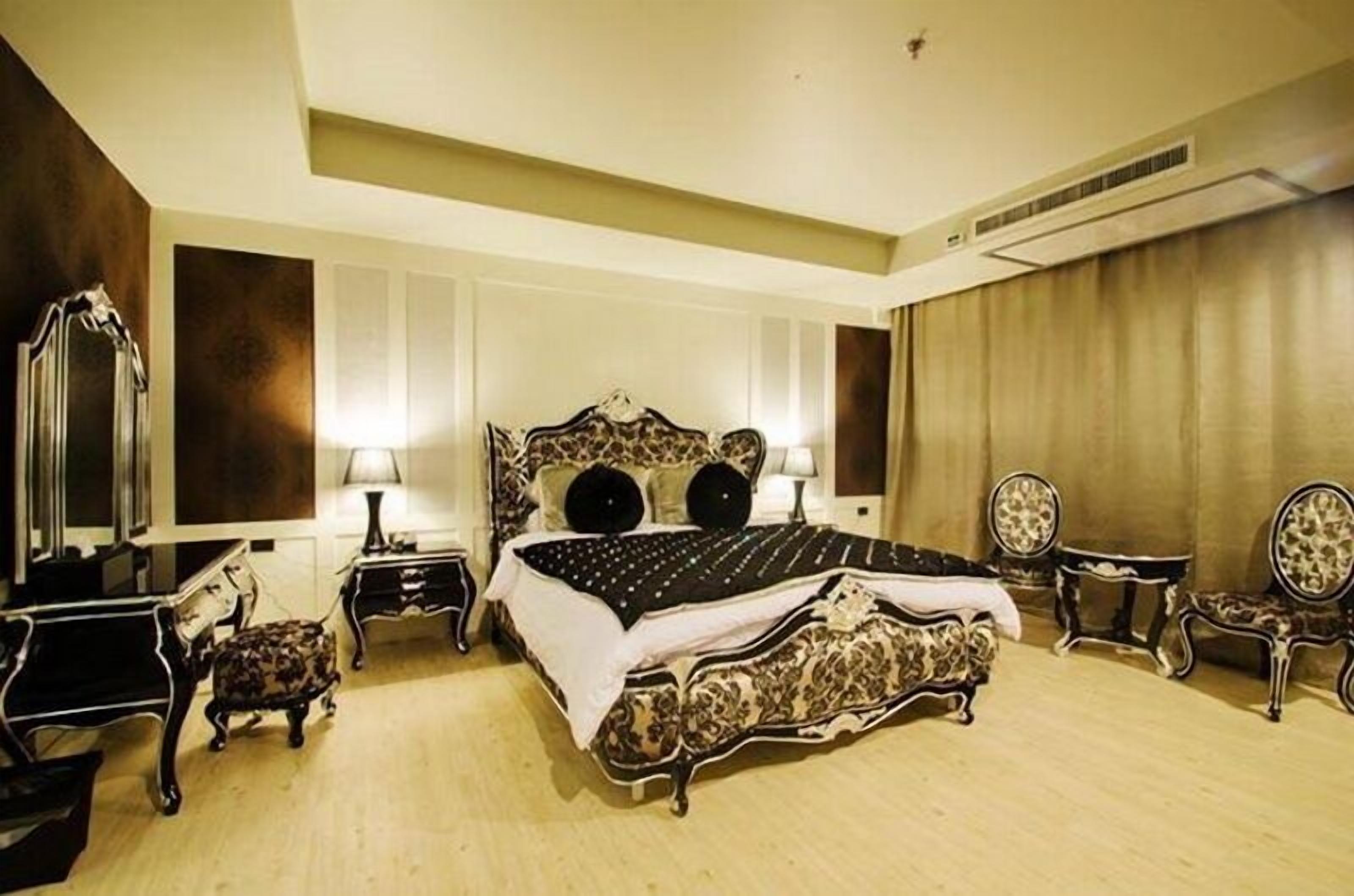 A spacious bedroom with a large bed, two bedside tables, a mirror, and two chairs.