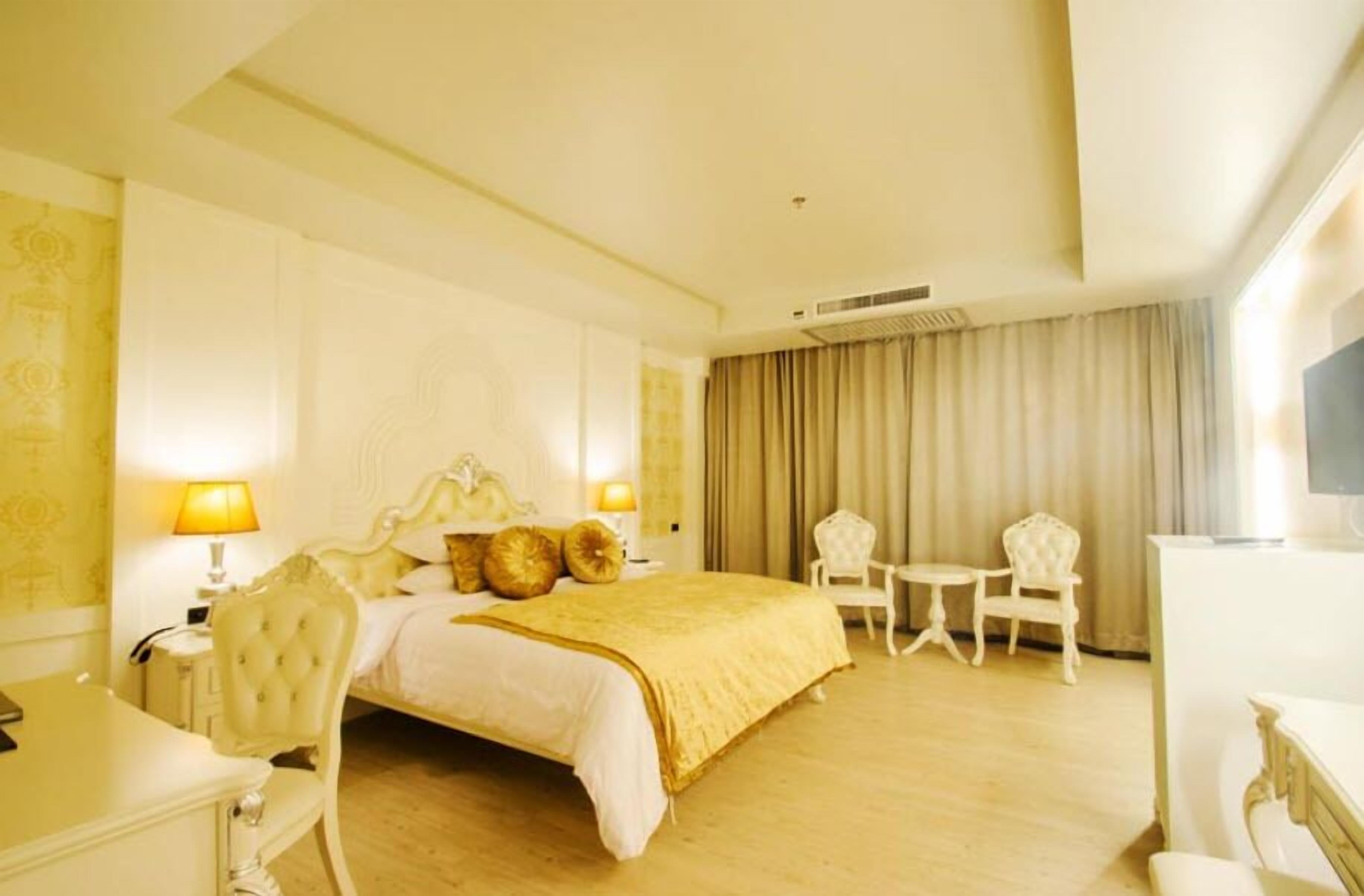 A hotel room with a large bed, two bedside lamps, a desk, and two chairs.