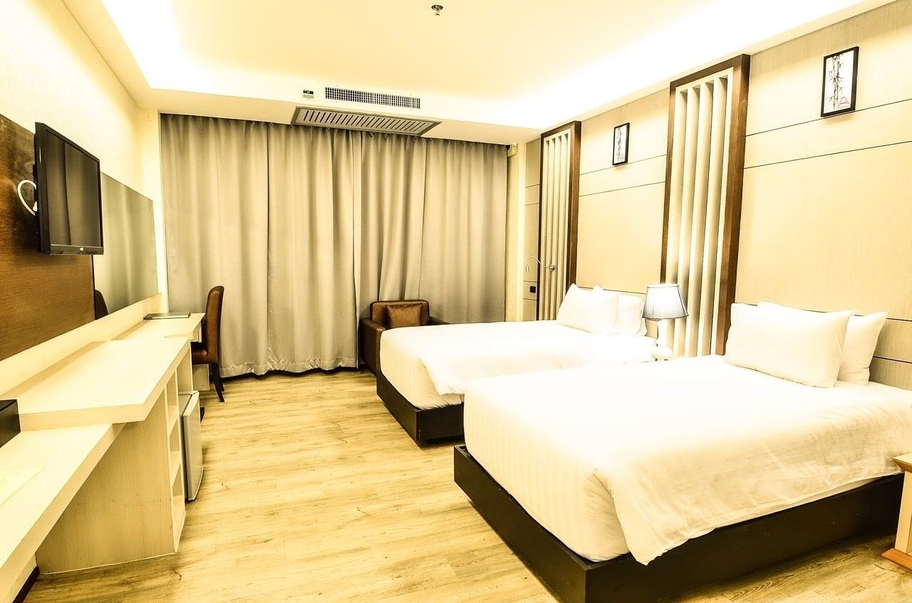 A hotel room with two beds, a desk, a chair, a TV, and a large window with curtains.