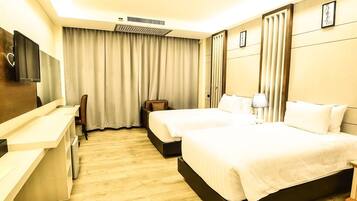 A hotel room with two beds, a desk, a chair, a TV, and a large window with curtains.