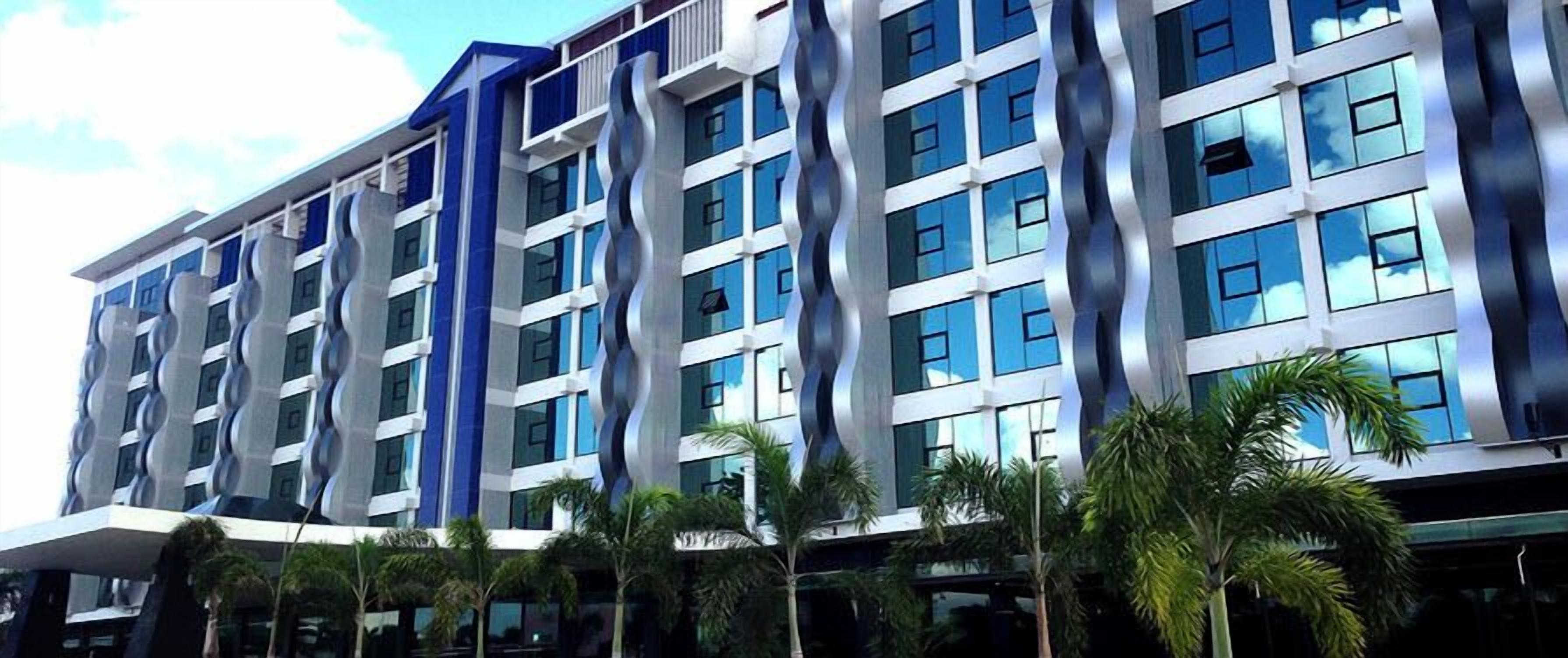 Un hotel moderno con una fachada ondulada, varios pisos y una hilera de palmeras en primer plano.