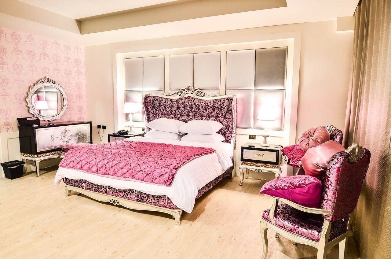 A bedroom with a large bed, two bedside tables, a vanity, and a chair.