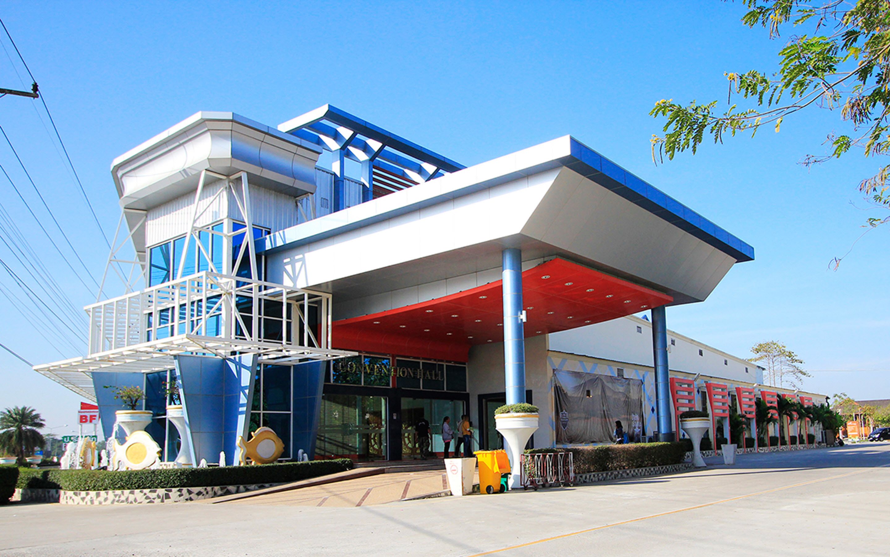 A modern building with a blue and white color scheme, a covered entrance, and a large planter with greenery.