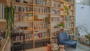 A room with a large bookshelf filled with books, a blue chair, and a small table with a lamp. - Motif No.1 Guest House (Paju)