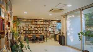 A library with bookshelves, reading tables, and potted plants. - Motif No.1 Guest House (Paju)