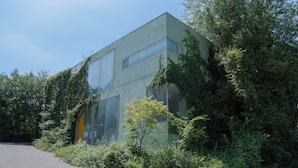 A building with large windows, surrounded by dense greenery and a paved area in front. - Motif No.1 Guest House (Paju)