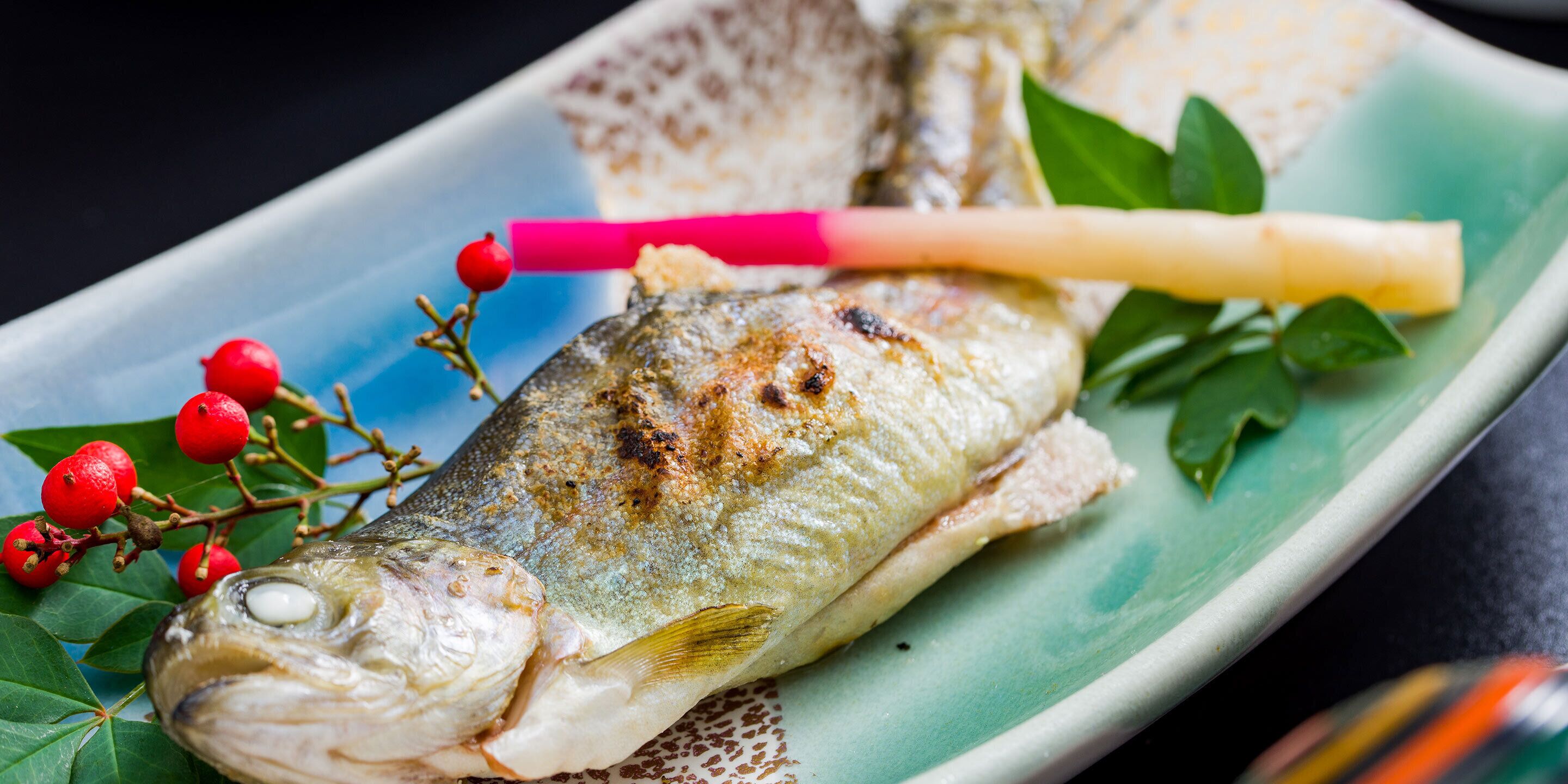 A grilled fish with a fork and a decorative branch with red berries on a plate.
