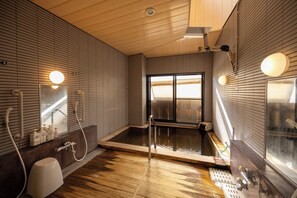 A modern bathroom with a wooden floor, a large bathtub, and a window providing natural light.