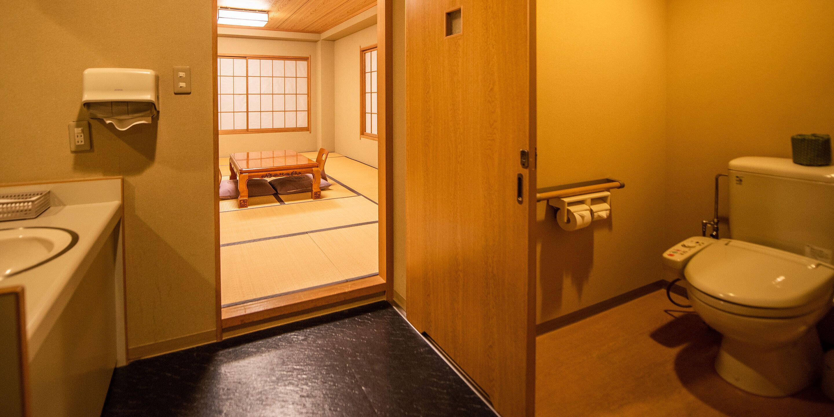 Ett traditionellt japanskt badrum med en toalett av trä, ett handfat och ett fönster med tatamimattor i bakgrunden.