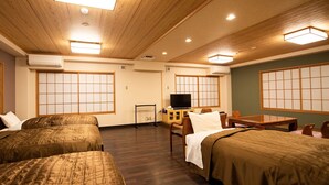 Habitación de hotel con dos camas, televisión, escritorio y puertas correderas tradicionales japonesas.
