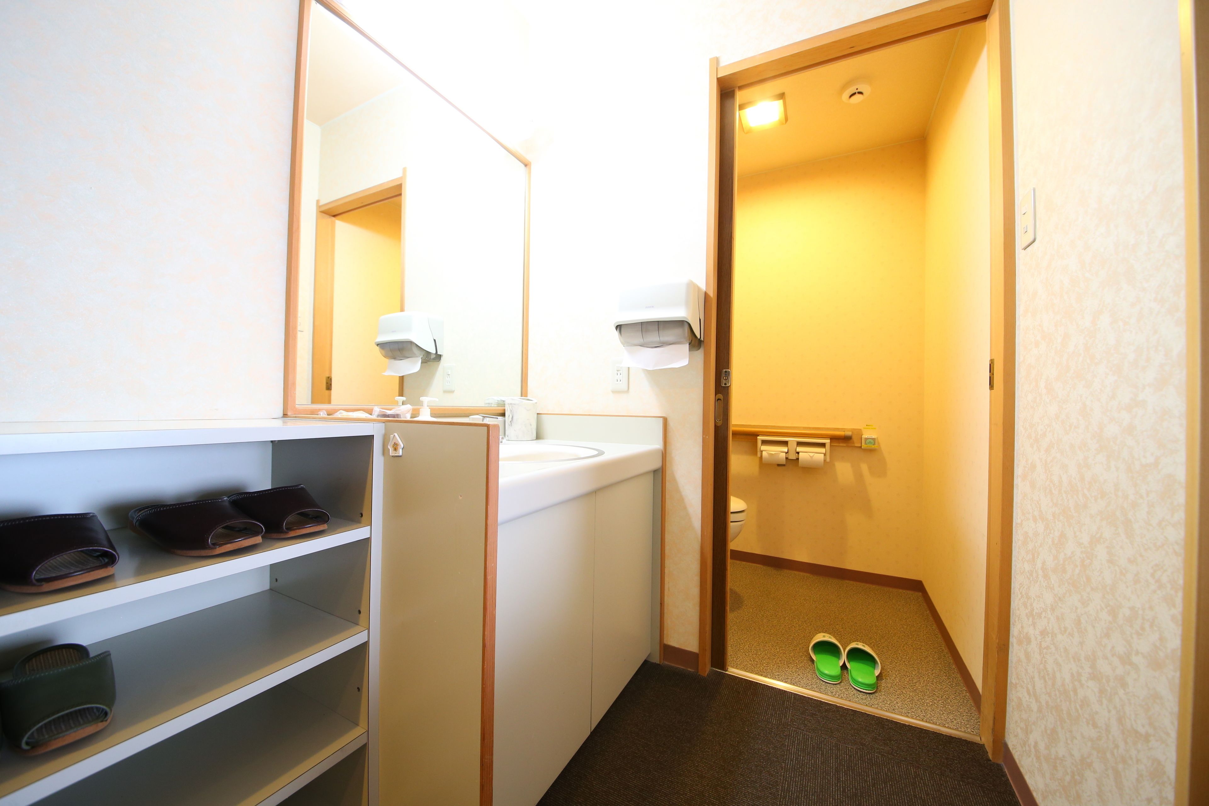 Un baño de hotel con lavamanos, espejo, estantes con zapatos y un inodoro.