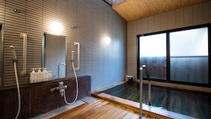 Un baño moderno con suelo de madera, un espejo grande y una bañera de hidromasaje con mampara de vidrio.