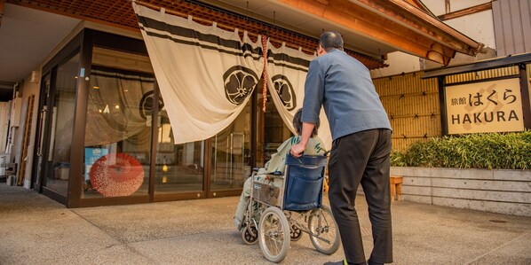 A man in a wheelchair outside a building with a sign reading "HAKURA".