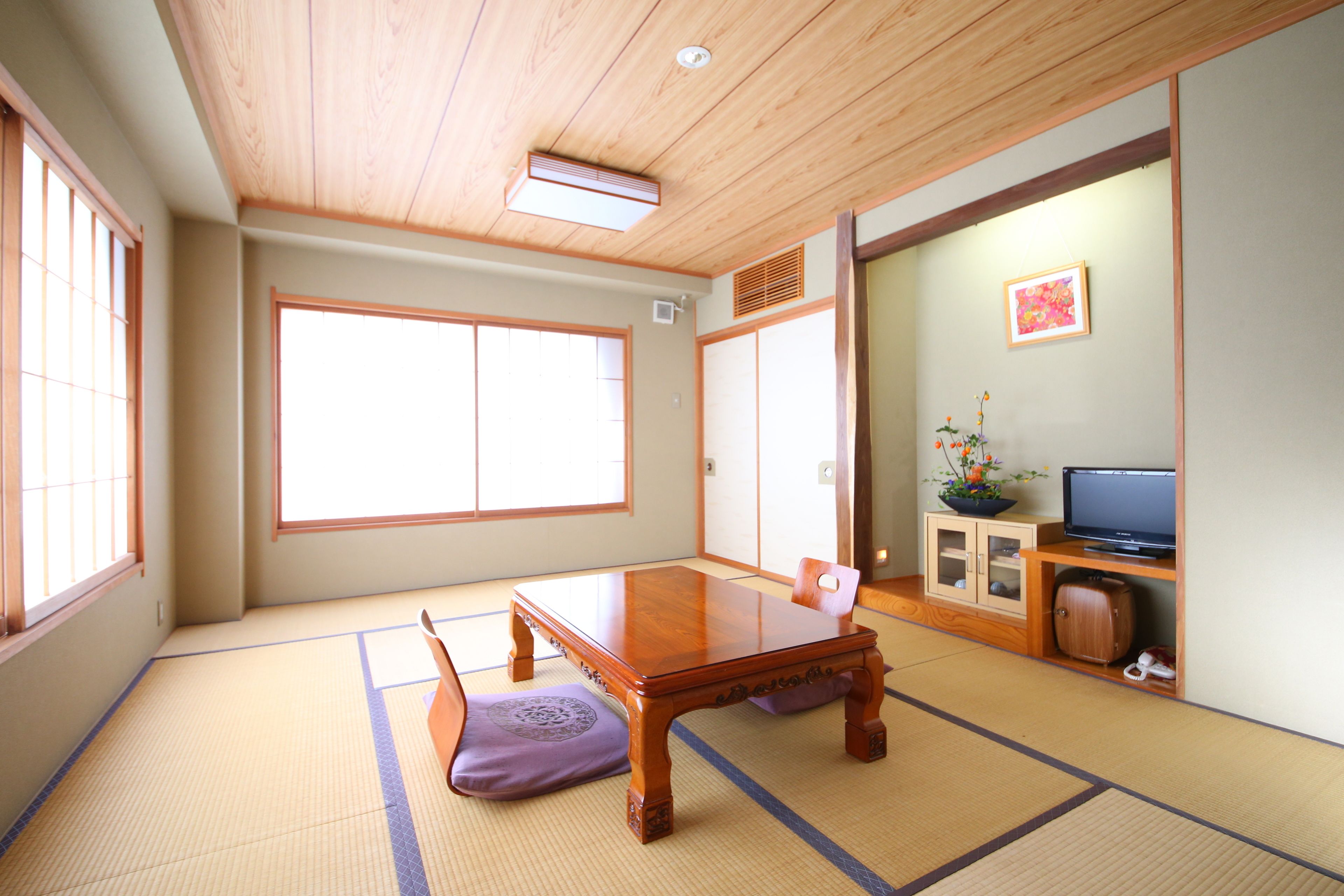 A traditional Japanese room with tatami flooring, a wooden table, a television, and a cabinet.