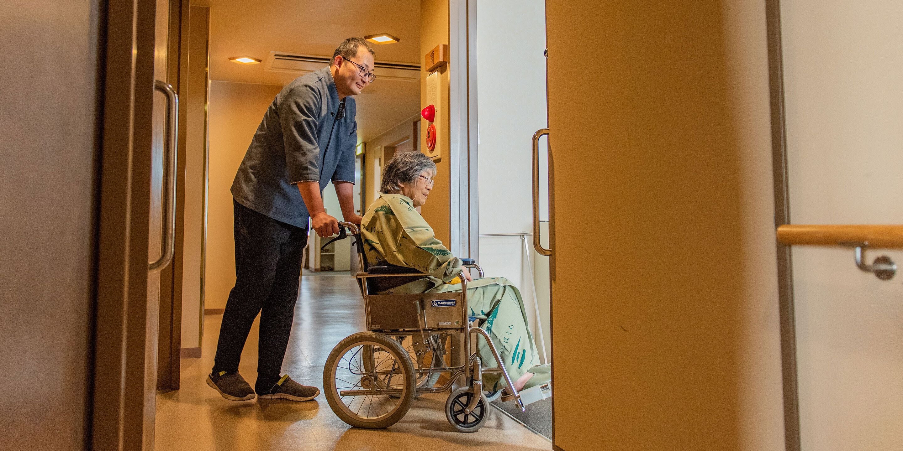 A corridor with a wheelchair and a person assisting.
