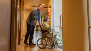 A corridor with a wheelchair and a person assisting.