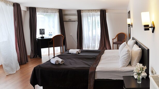 A hotel room with a large bed, a desk, two chairs, and a small table with a vase of flowers. - Hotel Corner (Tbilisi)