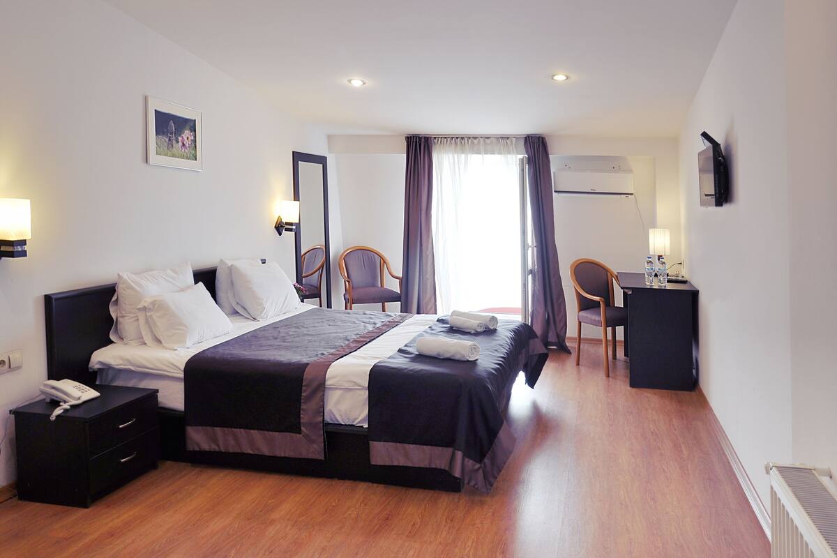A hotel room with a bed, bedside table, lamp, chair, desk, and a television.