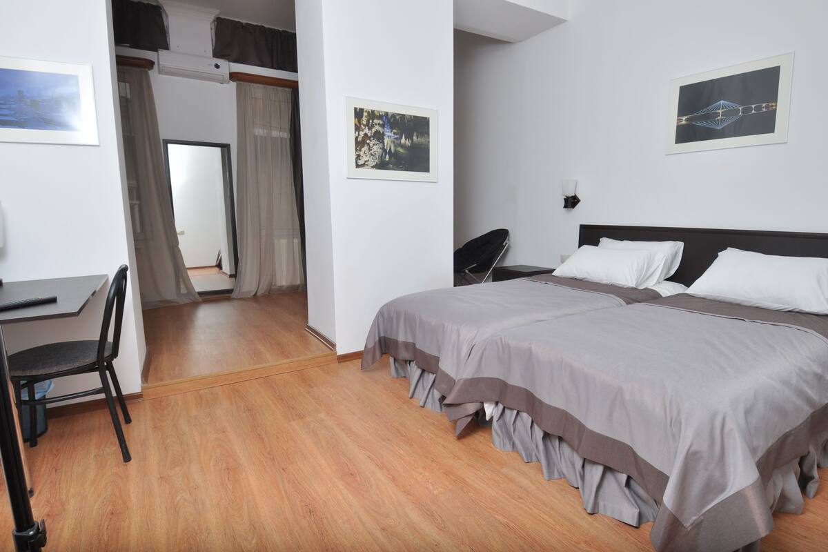 A hotel room with a bed, a desk, and a chair. There are two framed pictures on the wall.
